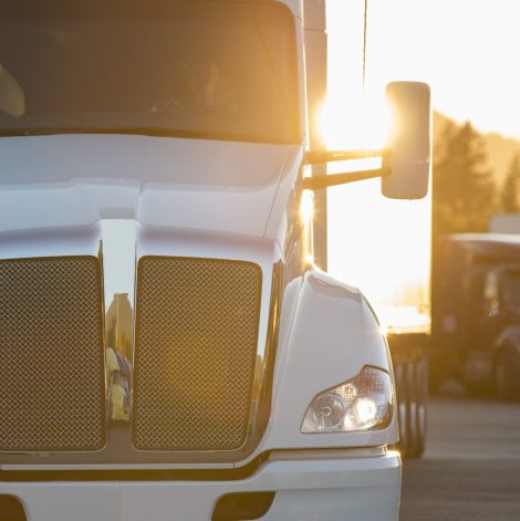 A large commercial truck moving through a truck stop parking lot at sunset.